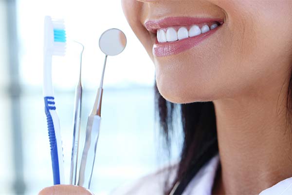 Dental hygienist holding a blue toothbrush and 2 dental cleaning instruments